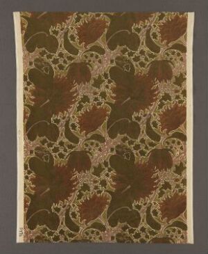  A piece of machine-woven cotton velvet textile named "Caladium" by Charles Francis Annesley Voysey, featuring a dark olive green twill weave base with a printed pattern of rust and golden botanical motifs, suggesting a historical Arts and Crafts influence.