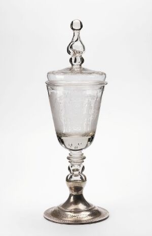  A clear glass goblet with a lid and a silver-colored node and base, against a light grayish-white background. The goblet displays a spherical finial on the lid, a textured bell-shaped bowl, and a circular base with delicate engravings.