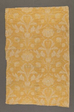  A rectangular aged yellow textile fragment with a repeated pale yellow botanical pattern, featuring symmetrical flower-like motifs surrounded by leaves, indicative of a historical fabric, possibly used for clothing or upholstery.