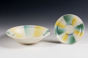  Two ceramic pieces, a shallow bowl and a plate, with a pastel marbled glaze in yellow, cream, green, and blue, displayed against a light grey to white gradient background.