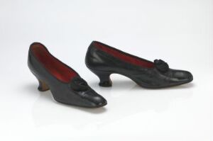  A pair of vintage black women's shoes with low heels and a decorative front, featuring a red interior lining, displayed against a neutral background.