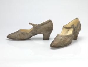  A pair of vintage taupe closed-toe women's shoes with a low strap and button detail on a light grey background, indicative of early to mid-20th-century fashion.