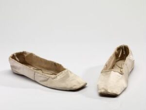  A pair of well-worn, off-white flat shoes with a pointed toe design, displayed against a neutral light grey background, illustrating signs of extensive use and simple fashion.