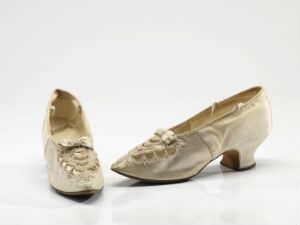  A pair of vintage creamy beige women's shoes with low curved heels, decorated with intricate lace and beadwork, displayed against a white background.