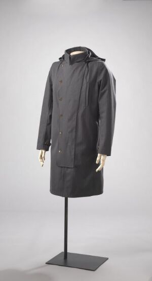  A dark grey, double-breasted trench coat displayed on a mannequin stand against a light grey background.