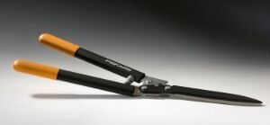  A pair of orange-handled Fiskars garden shears with black blades, positioned diagonally against a gradient gray background. The tool is designed for trimming trees and shrubs, and the molded plastic and metal construction is indicative of the Fiskars brand.