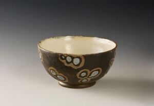  A handcrafted ceramic bowl with a dark brown exterior featuring white circular motifs and a creamy white interior, displayed on a softly focused neutral background.