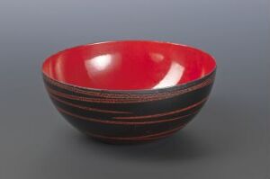  A bowl designed by Grete Prytz Kittelsen with the title "Prikkedekor," crafted from iron and enamel. The exterior is black with muted red horizontal stripes, while the interior boasts a reflective, vibrant red color.