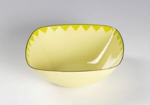  A stainless steel shallow bowl designed by Grete Prytz Kittelsen with a vibrant yellow enamel-coated interior, featuring triangular yellow tips on the rim against a gentle gray or off-white background.