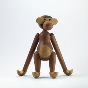  A wooden articulated monkey figure with a warm brown tone and visible wood grain, sitting with legs apart and arms resting down, against a plain white background.