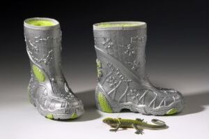  A pair of children's boots in grey and lime green with a futuristic, nature-inspired design, along with a matching toy lizard, designed by Sigrid Eckhoff, against a neutral background.