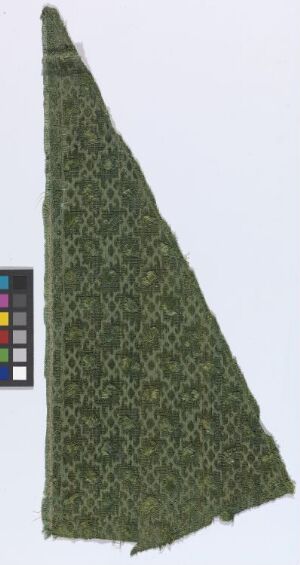  A detailed image of a triangular fragment of fabric with a dense, dark green vegetal pattern on a light background, featuring an irregular cut along one side and a color chart in the corner for reference.