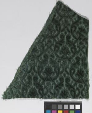  A fragment of ornate dark green fabric with swirl patterns, with a color calibration chart at the bottom. Artist name and title are unknown.