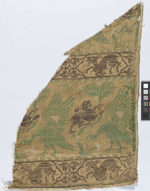  A damaged, triangular-shaped historic fabric fragment with a muted olive-green background, featuring a leaping golden-tan lion and intricate scrolling vine motifs, conveying a medieval or Renaissance aesthetic.