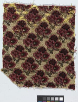  A photograph of an intricately patterned textile with a rich floral design in maroon and gold on a dark background, displaying signs of fraying at the edges and including a color scale reference below.