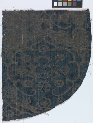  A fragment of an ancient textile with a faded, intricate floral design in shades of dark and light blue, set against a light gray background with a color scale reference above.