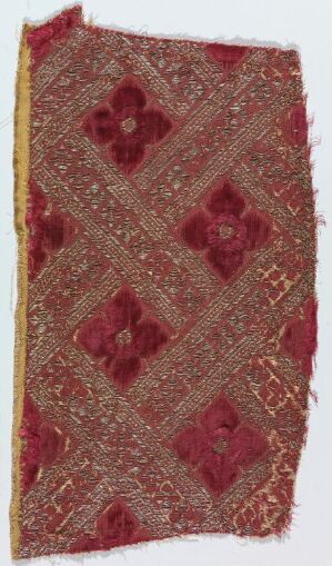  Antique textile fragment featuring a red and gold diamond pattern with a central floral motif within each diamond, exhibiting intricate gold threadwork and slight fraying at the edges, suggesting historical significance and handcrafted skill.