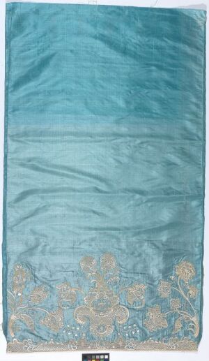  A vertically oriented piece that looks like a fabric art with a light turquoise top transitioning to a patterned bottom with metallic floral motifs against a blue background.