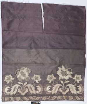  An ornate, antique-looking aubergine-colored textile panel featuring a horizontal band of creamy beige floral patterns at the lower section, with a plain, dark plum fabric above separated by a horizontal seam.