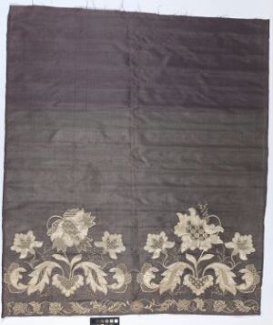  A rectangular dark grey textile with decorative off-white floral embroidery at the bottom, exhibiting a traditional design and a natural color contrast, possibly intended for interior decoration. Artist name and title are unknown.