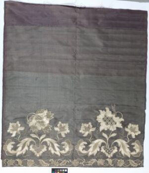  A textile piece with a dark gray background and intricate cream-colored embroidered floral designs at the bottom.