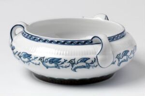  An elegant feldspar porcelain piece titled "Modell 2004" by Porsgrunds Porselænsfabrik AS, featuring a glossy white finish with underglaze cobalt blue floral and geometric patterns along the rim and handles, as well as sparser blue motifs on the sides, with a broad opening and gracefully protruding handles.