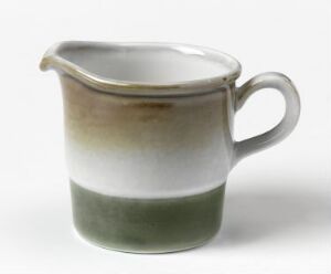  A small ceramic creamer jug with a dual-toned glaze; the lower half is a muted green while the upper half is an off-white with gray hints. The jug has a rounded handle and a spout, set against a plain background.