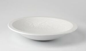  A shallow feldspar porcelain plate designed by Porsgrunds Porselænsfabrik AS, featuring a subtle embossed design at the center, displaying a smooth and glossy terralenglasur finish, set against a soft light grey background.