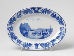  An oval-shaped ceramic plate by Egersunds Fayancefabrik with a central blue and white harbor scene surrounded by a decorative border of stylized foliage in varying shades of blue. The title is unknown, but the piece is indicative of the 264.2 classification in dining and eating utensils from the decorative arts category, featuring cast and glazed flint clay with pressed decoration.