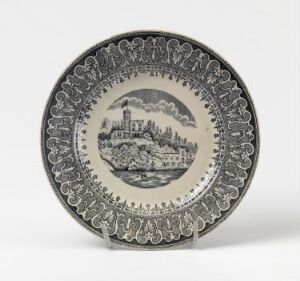  A decorative earthenware plate titled "Unionen" by Egersunds Fayancefabrik, featuring a grayscale village scene with an intricate border, displayed on a stand, showcasing a neutral palette of gray and off-white.