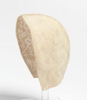  A delicate off-white lace cap with floral patterns on a stand against a light grey to white gradient background.