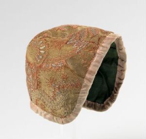  A vintage cap with a detailed peach-colored tapestry pattern featuring green, blue, red, yellow, and light gray floral embroidery, a pale beige satin edging, and dark green interior lining.