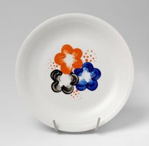  A feldspar porcelain plate designed by Randi Gulbrandsen, featuring a trio of hand-painted enamel flowers in orange, black, and blue with specks of red and blue on a white background.