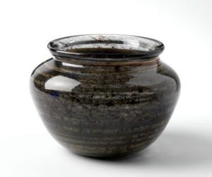  A blown glass object titled "Den arkaiske serie / K-4088" by Arne Jon Jutrem, featuring a rounded form with semi-opaque deep grey color and speckles of white and lighter grey, set against a plain background. The piece exemplifies fine crafts design and boasts a texture of carefully integrated color speckles.