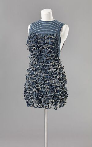  An Armando E. Santos-designed costume on a mannequin, featuring a sleeveless top with blue horizontal stripes and a lower section resembling blue chain mail, crafted from machine-woven cotton and silk.