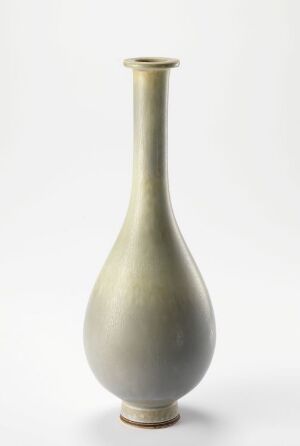  An elegant slender ceramic vase with a pale green to earthy toned gradient, displaying a smooth and organic shape against a light grey background. Artist name and title are unknown.