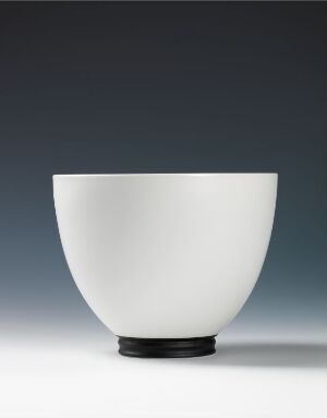  A white ceramic bowl with a smooth, curved shape and a contrasting black base sitting against a graduated grey-blue background. Artistname and title are unknown.