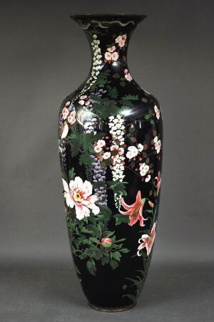  A tall black vase with a glossy finish, decorated with a vibrant floral pattern in shades of pink, white, and green, set against a plain background.