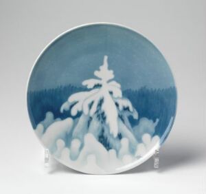  A blue and white hand-painted porcelain plate by Porsgrunds Porselænsfabrik AS, featuring a central snow-covered tree against a backdrop of a blue gradient forest line under a lighter blue sky.