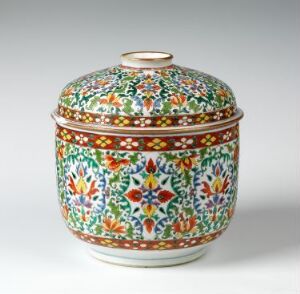  A round, intricately decorated porcelain container known as "Bencharong" by an unknown artist, featuring overglaze enamel decoration in rich colors such as green, blue, and orange with detailed floral and geometric patterns, displaying traditional craftsmanship in porselen tableware.