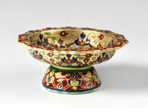  A small footed Bencharong bowl with intricate overglaze enamel decoration in vibrant colors and gold outlines, with an off-white background, and complex patterns featuring mythical creatures and floral motifs. Artist unknown.