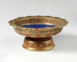  An ornate Bencharong porcelain bowl with a scalloped, gilded edge, intricately decorated with traditional Thai multi-colored enamel patterns on its exterior, and featuring a rich cobalt blue interior with gold detailing. The bowl rests on a matching, patterned gold pedestal. Artistname is Ukjent.