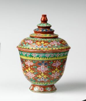  An intricately painted Bencharong porcelain jar and lid with vibrant floral patterns in red, green, blue, yellow, and pink overglaze enamel colors, representative of traditional Thai artistry. The artist is unknown.