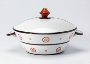  A white feldspar porcelain serving dish with a lid, designed by Nora Gulbrandsen, featuring a pattern of small red dots encircled by darker rings and a tiered handle with orange and red accents on the lid.