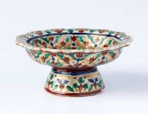  A Bencharong porcelain bowl with a flared rim, adorned with intricate over-glaze enamel decoration in green, blue, russet, and yellow, highlighted with red and gold lines, displaying traditional Thai craftsmanship. Artist unknown.