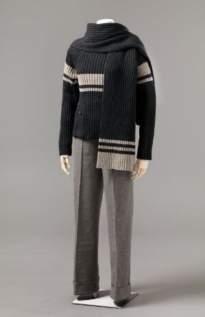  A mannequin dressed in an elegant black and beige-striped sweater with a high turtleneck and sleek grey trousers, set against a simple grey background.