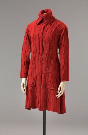  A deep red, textured, long-sleeved knee-length coat with a high neck and large patch pockets, displayed on a featureless mannequin against a neutral grey background.