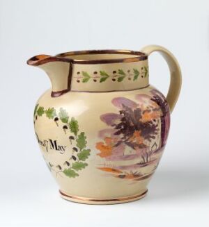  A ceramic pitcher with a creamy beige base color, decorated with a vibrant floral design featuring a large purple flower, green foliage, and the word "May." The upper rim and handle are highlighted with a brownish glaze.