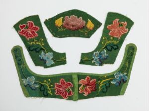  Four pieces of traditional green textile with red, pink, and blue floral embroidery, likely parts of a costume or uniform, against a white background.