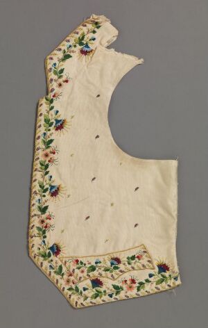  An antique, asymmetrical piece of cream-colored fabric with a scalloped hem and detailed floral embroidery in red, blue, green, and yellow along the edges, displayed against a neutral gray background.